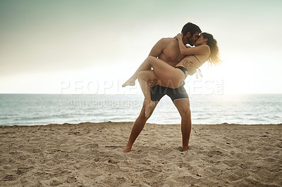 Buy stock photo Shot of a young man holding his girlfriend on the beach