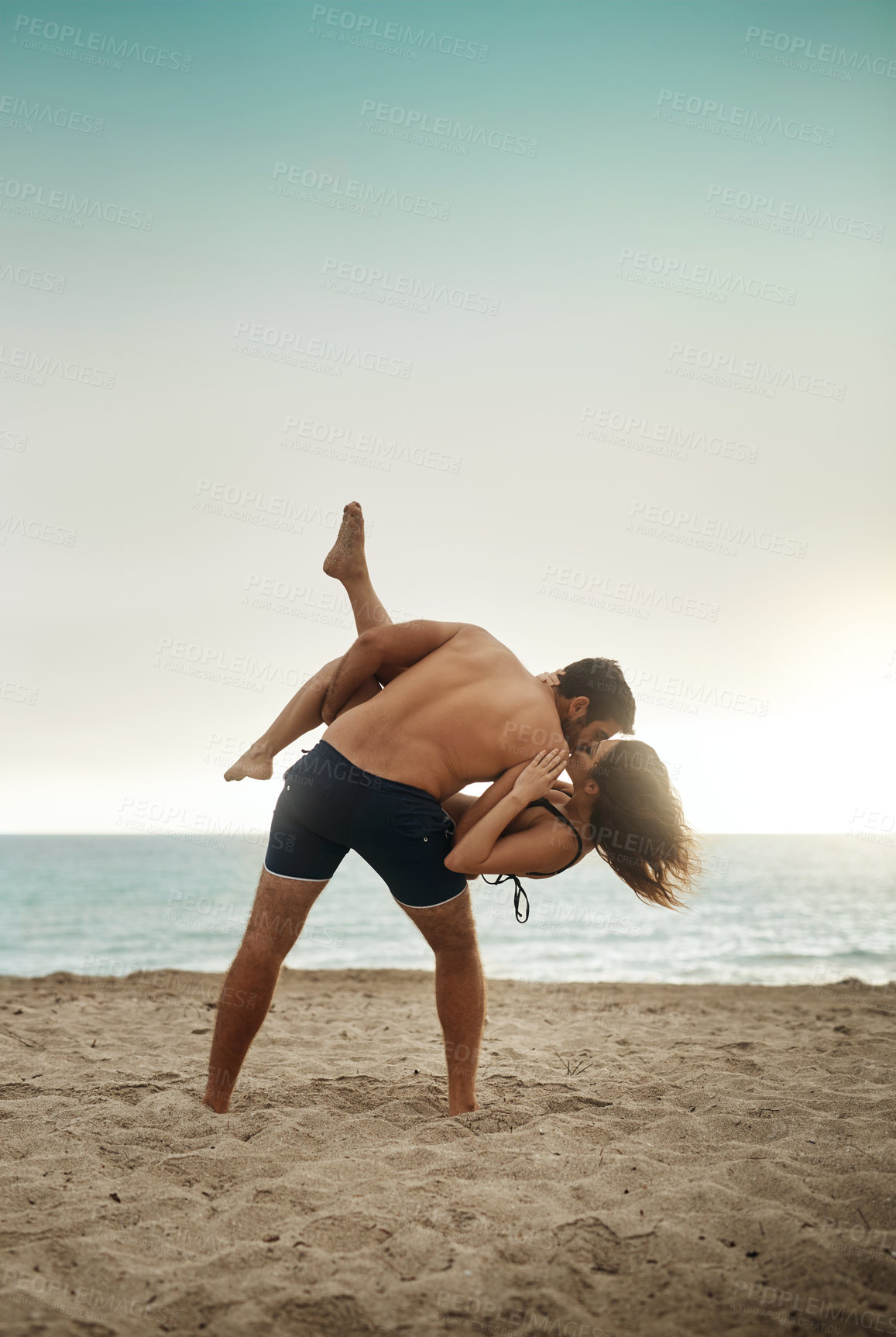 Buy stock photo Shot of a young man holding his girlfriend on the beach