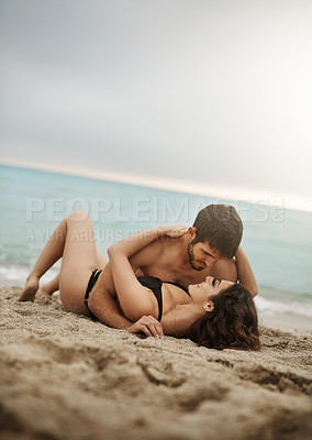Buy stock photo Shot of an affectionate couple laying lovingly on the beach