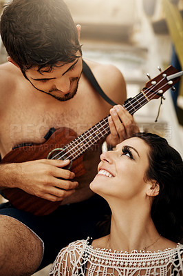 Buy stock photo Shot of a young couple playing the ukulele on the beach