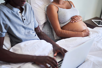 Buy stock photo Defocused shot of a man using his laptop while sitting in bed with his pregnant wife