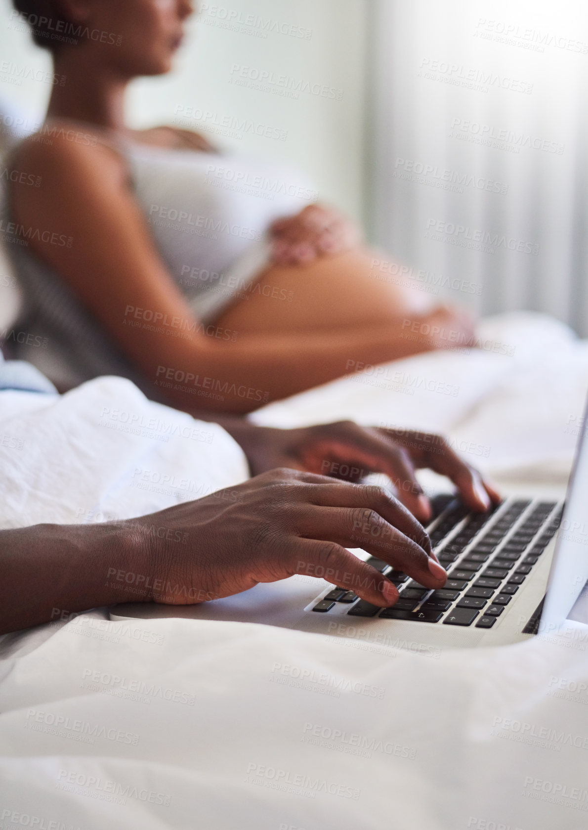 Buy stock photo Defocused shot of a man using his laptop while sitting in bed with his pregnant wife