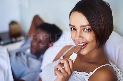 Buy stock photo Shot of a young woman enjoying a chocolate while lying in bed with her husband