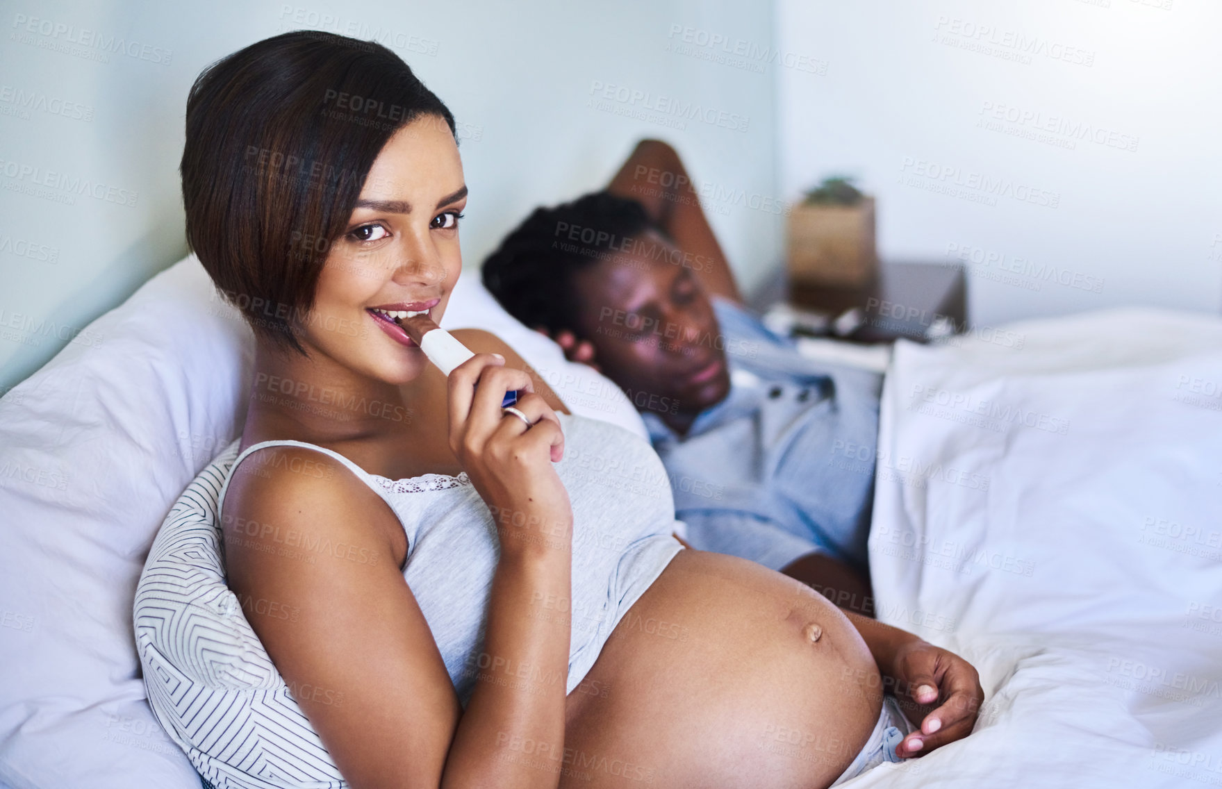 Buy stock photo Cropped shot of a pregnant woman enjoying a chocolate while lying in bed