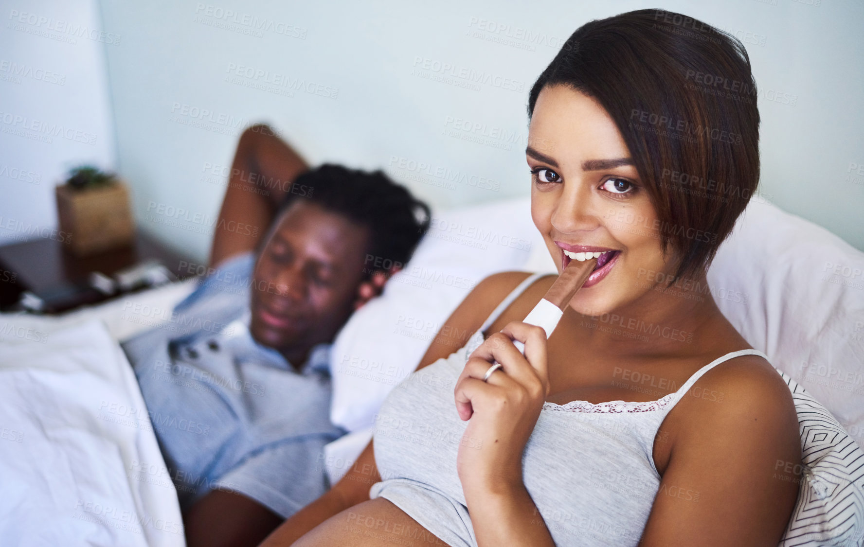 Buy stock photo Cropped shot of a pregnant woman enjoying a chocolate while lying in bed