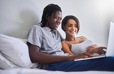 Buy stock photo Shot of a young couple using a laptop while lying in bed