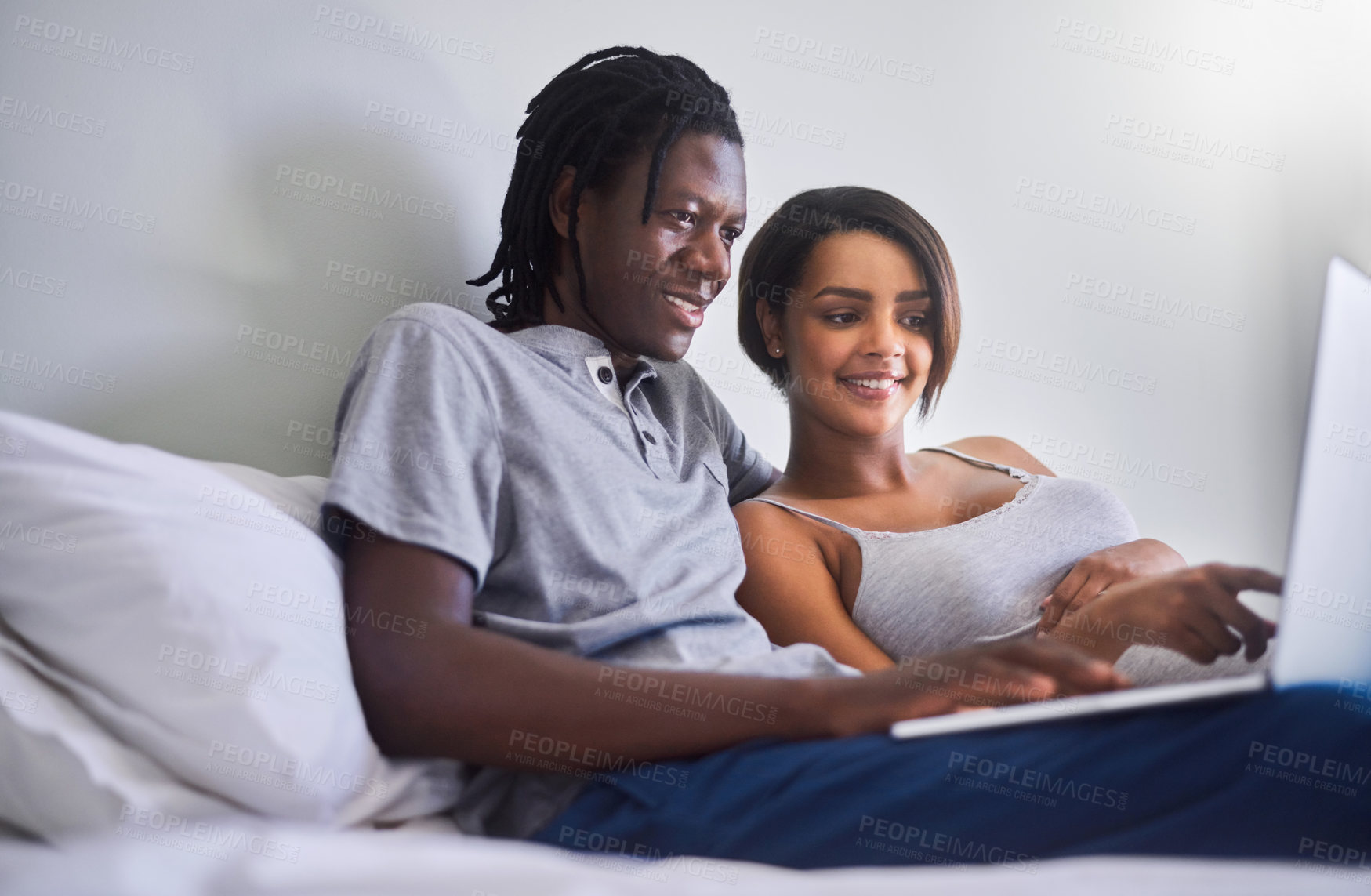 Buy stock photo Shot of a young couple using a laptop while lying in bed