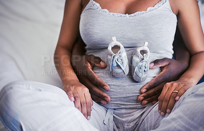 Buy stock photo Shot of a woman with baby shoes on her pregnant belly while sitting with her husband