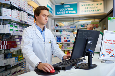 Buy stock photo Shot of a young pharmacist working on a computer in a chemist