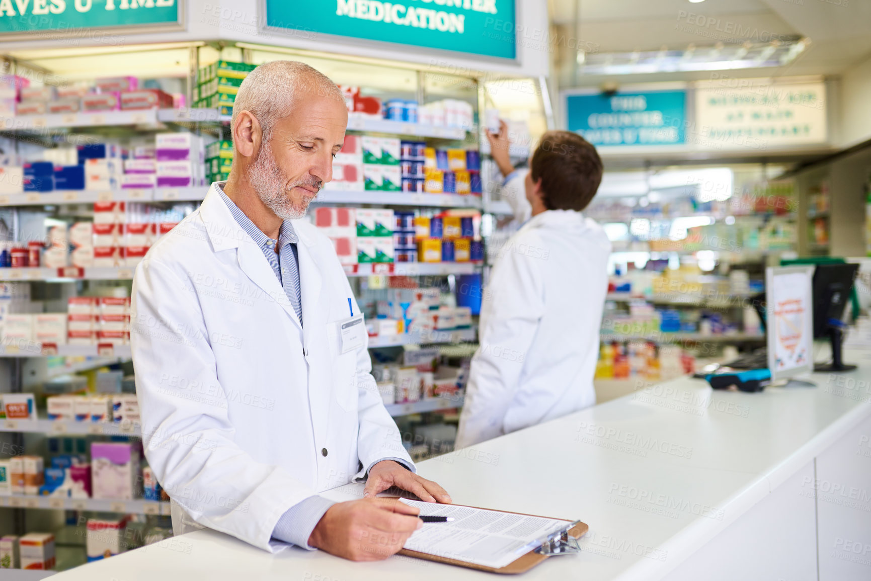 Buy stock photo Shot of a mature pharmacist writing on a clipboard in a chemist