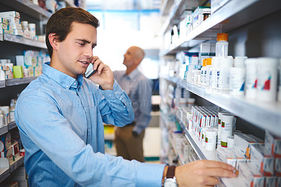 Buy stock photo Cropped shot of a handsome young man making a phonecall while looking for medication in a pharmacy