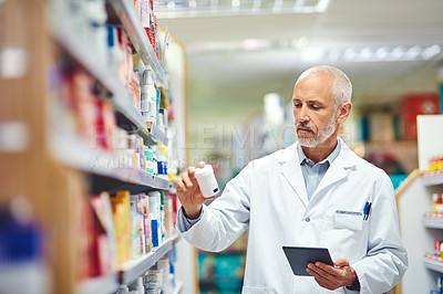 Buy stock photo Cropped shot of a handsome mature male pharmacist using a tablet while working in the pharmacy