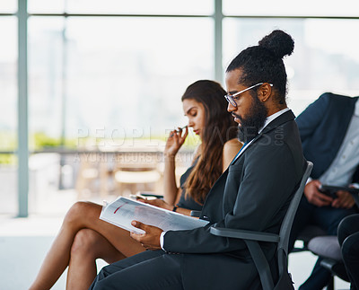 Buy stock photo Shot of a handsome young businessman reading through some paperwork during a seminar in the conference room