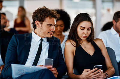 Buy stock photo Cropped shot of two young businesspeople using their cellphones during a seminar in the conference room