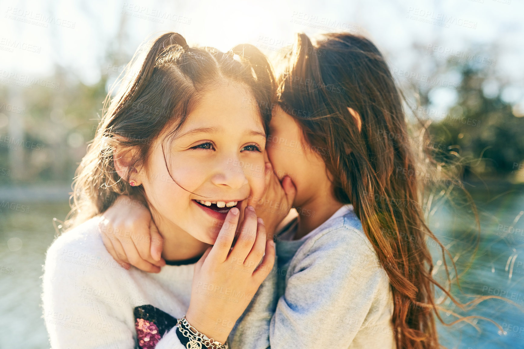 Buy stock photo Cropped shot of an adorable little girl whispering in her sisters ear outdoors