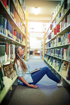Buy stock photo Shot of a university student sleeping between the bookshelves in the library at campus