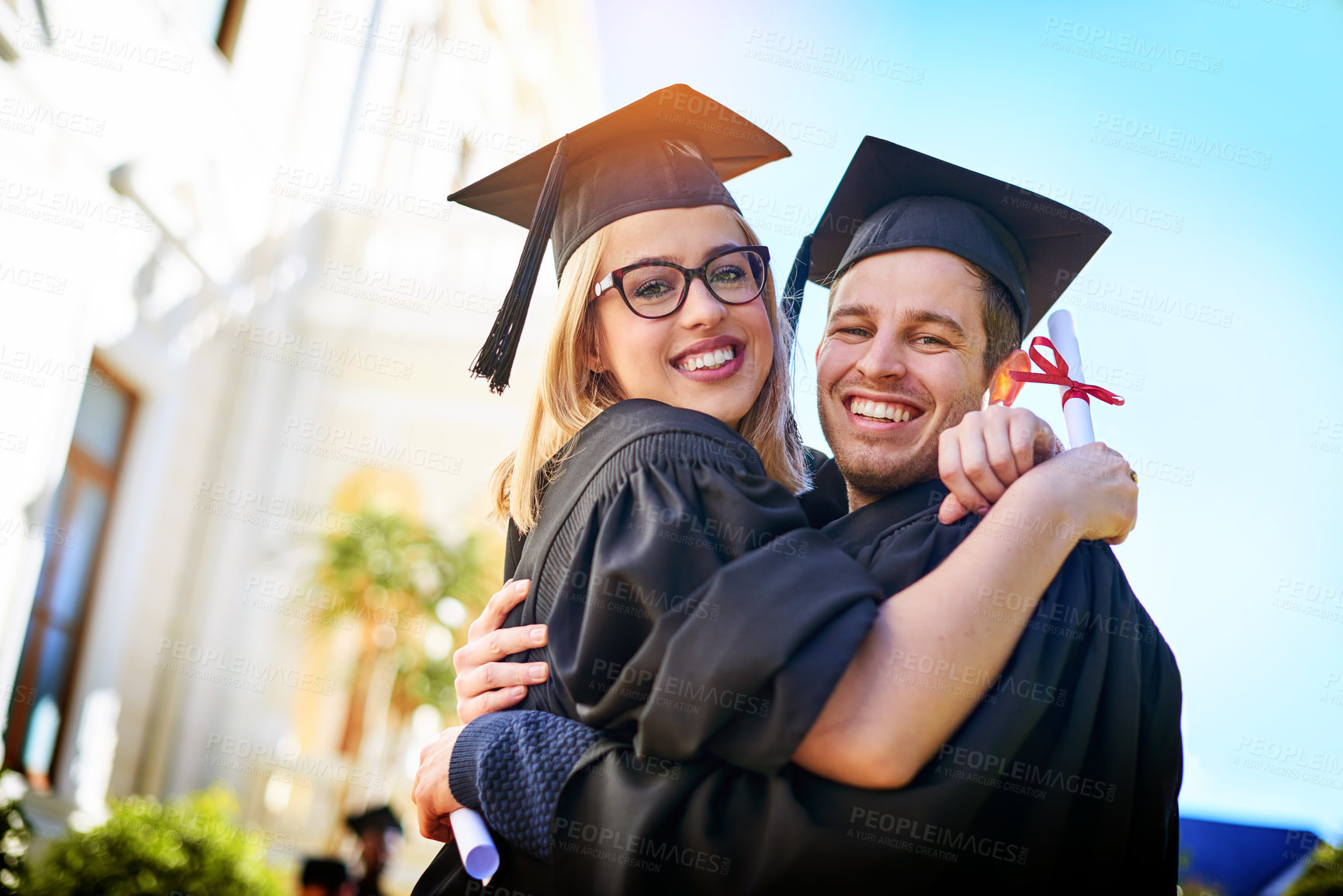 Buy stock photo Shot of a young couple embracing each other on graduation day