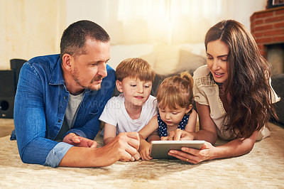 Buy stock photo Shot of an adorable brother and sister using a digital tablet with their parents on the floor at home