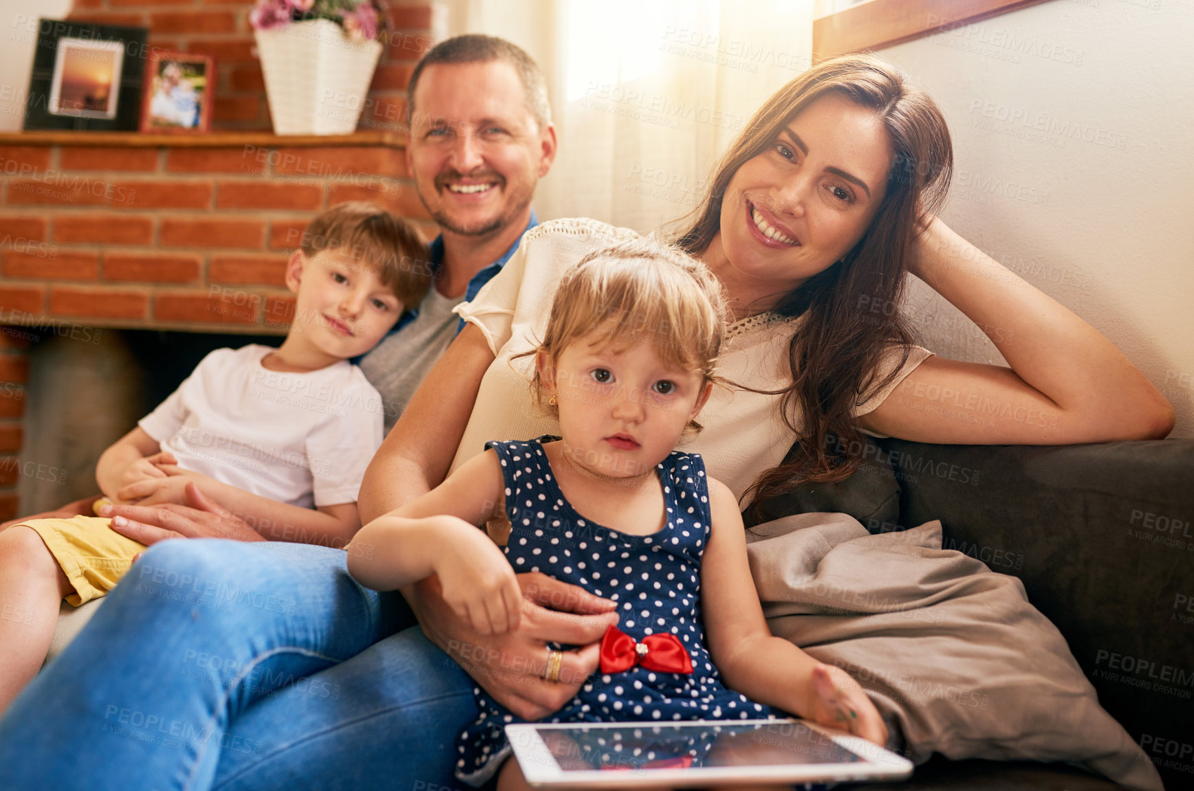 Buy stock photo Portrait of a happy young family of four relaxing together on the sofa at home