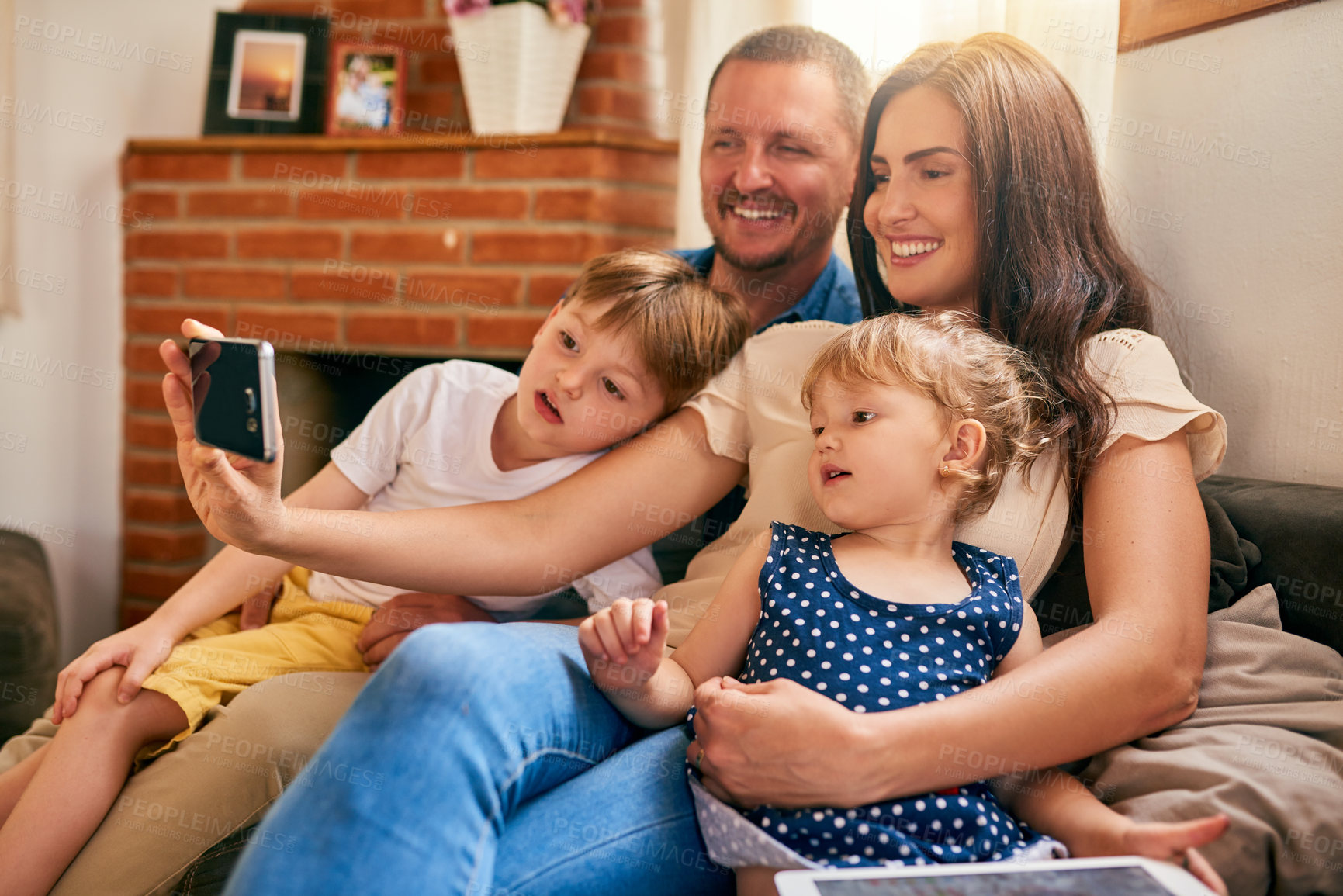 Buy stock photo Shot of a happy young family taking a selfie together on the sofa at home