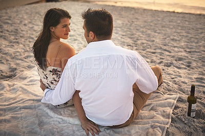 Buy stock photo High angle shot of an affectionate young couple sitting face to face on the beach