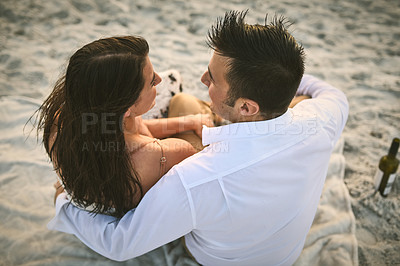 Buy stock photo High angle shot of an affectionate young couple sitting face to face on the beach
