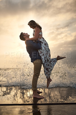 Buy stock photo Full length shot of a handsome young man picking up his girlfriend while standing on the jetty at the beach