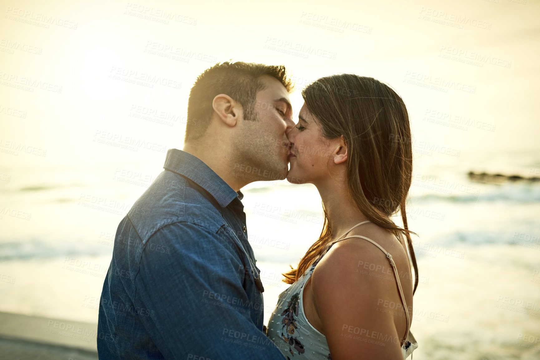 Buy stock photo Cropped shot of an affectionate young couple kissing while standing on the beach