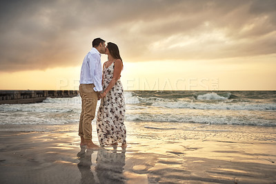 Buy stock photo Full length shot of an affectionate young couple kissing while standing on the beach