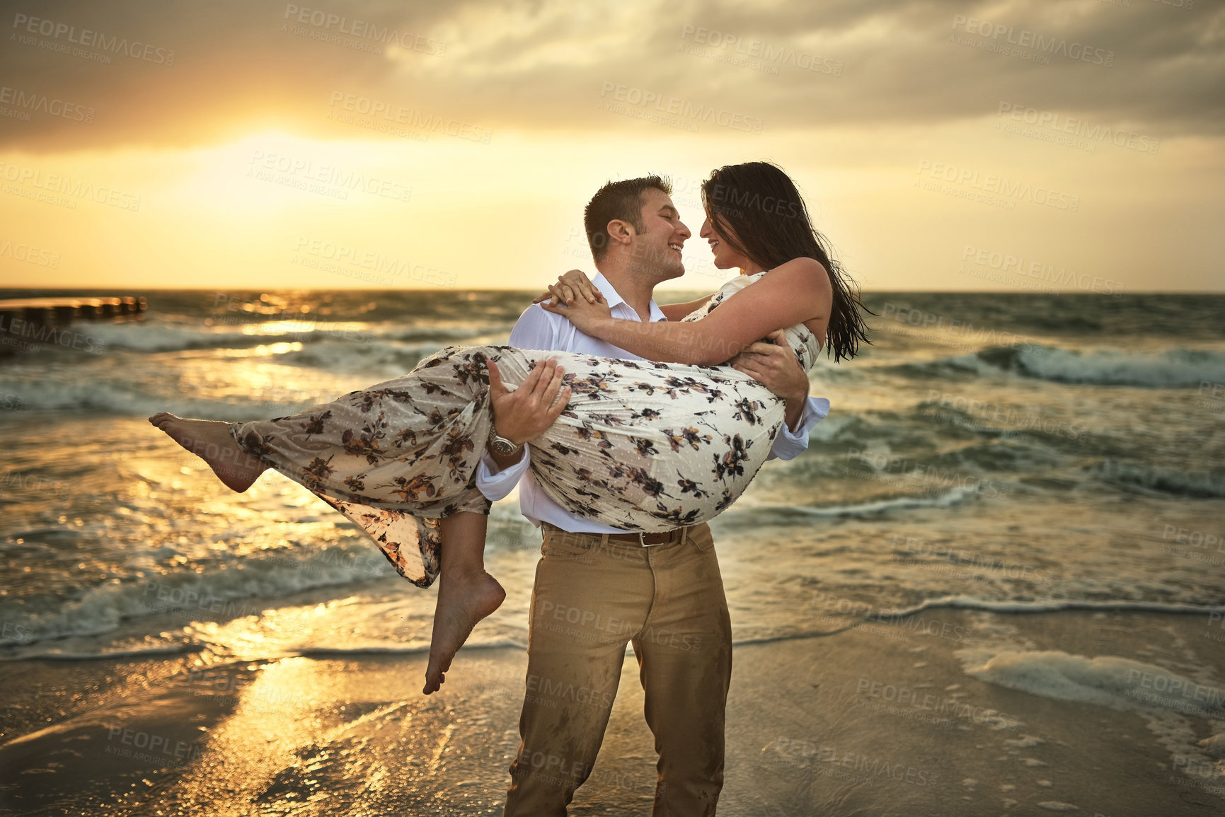 Buy stock photo Cropped shot of a handsome young man carrying his girlfriend on the beach