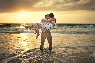 Buy stock photo Full length shot of a handsome young man kissing his girlfriend while carrying her on the beach