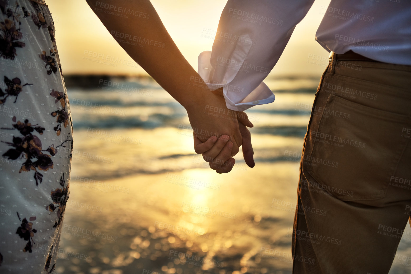 Buy stock photo Rearview shot of an unrecognizable couple holding hands while standing on the beach
