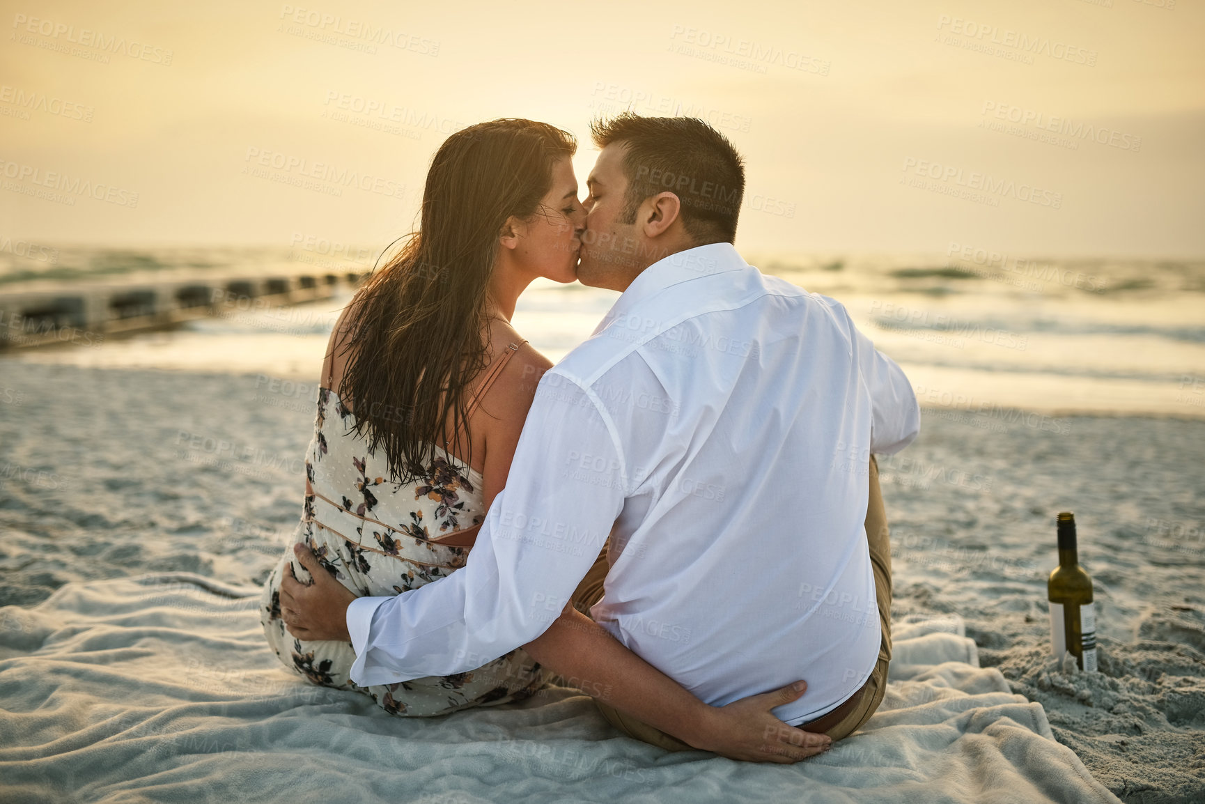 Buy stock photo High angle shot of an affectionate young couple kissing while sitting on the beach