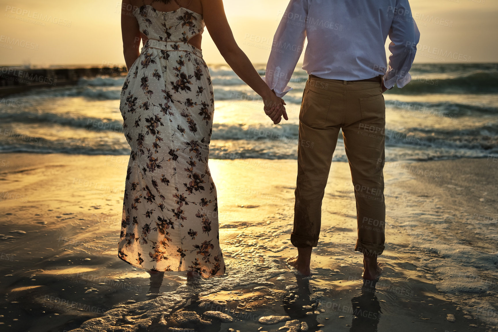 Buy stock photo Rearview shot of an unrecognizable couple holding hands while standing on the beach
