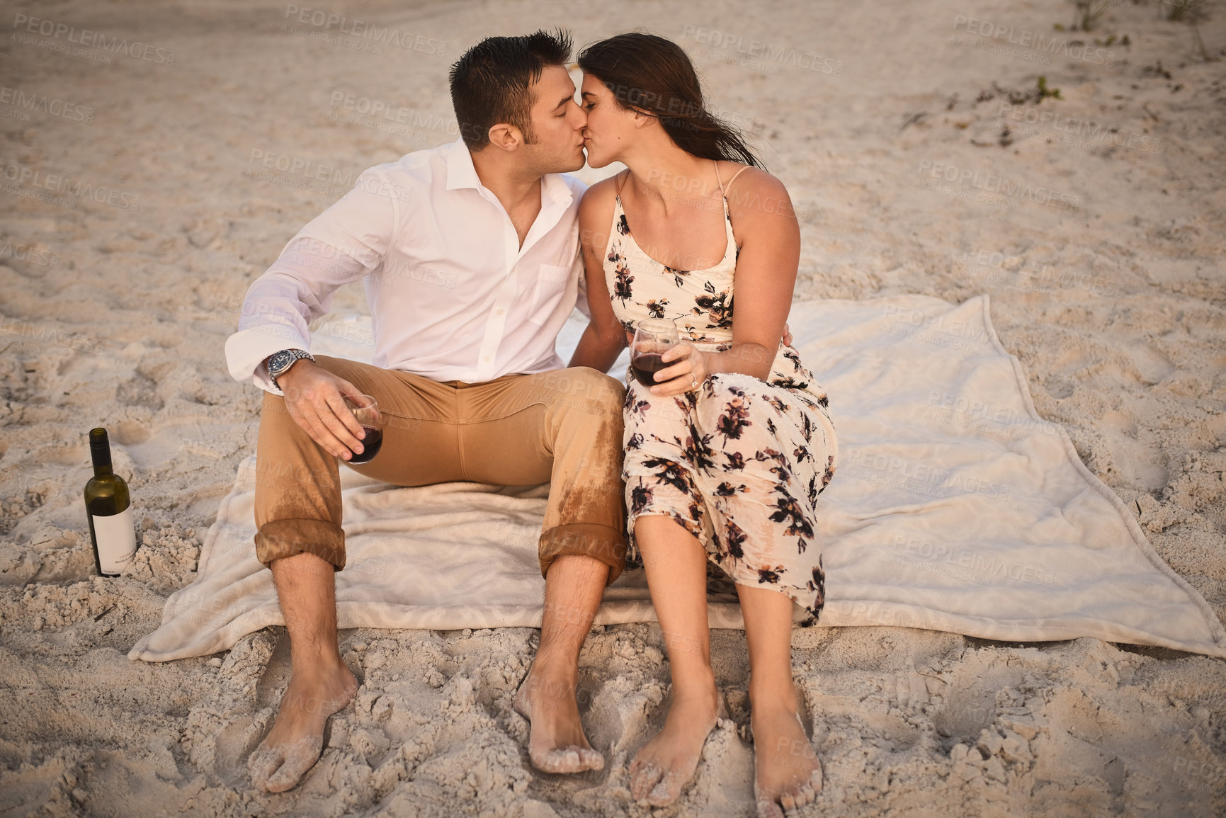 Buy stock photo High angle shot of an affectionate young couple kissing while sitting on the beach