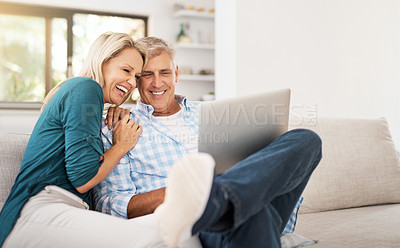 Buy stock photo Shot of an affectionate mature couple using a laptop while sitting on the sofa together at home