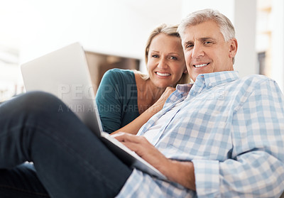 Buy stock photo Portrait of an affectionate mature couple using a laptop while sitting on the sofa together at home