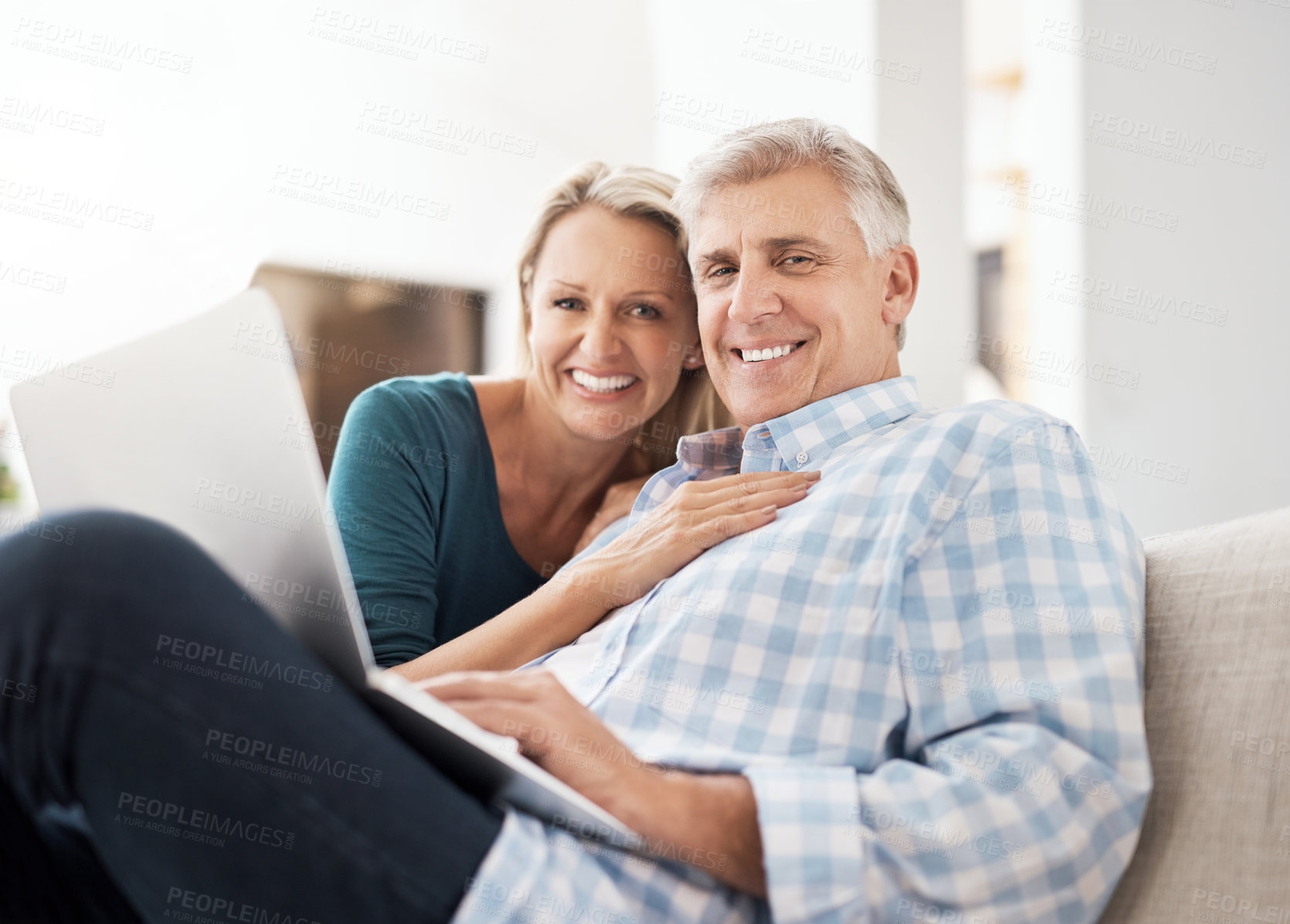 Buy stock photo Portrait of an affectionate mature couple using a laptop while sitting on the sofa together at home