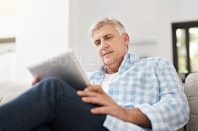 Buy stock photo Cropped shot of a handsome mature man using a tablet while sitting on the sofa at home