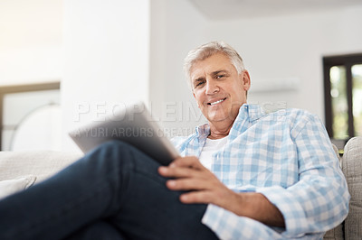 Buy stock photo Cropped portrait of a handsome mature man using a tablet while sitting on the sofa at home