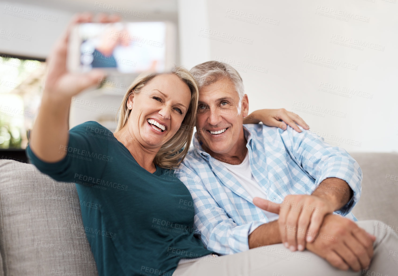 Buy stock photo Cropped shot of an affectionate mature couple taking selfies together while sitting on the sofa at home