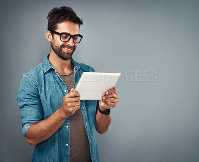 Buy stock photo Studio shot of a handsome young man using a digital tablet against a grey background