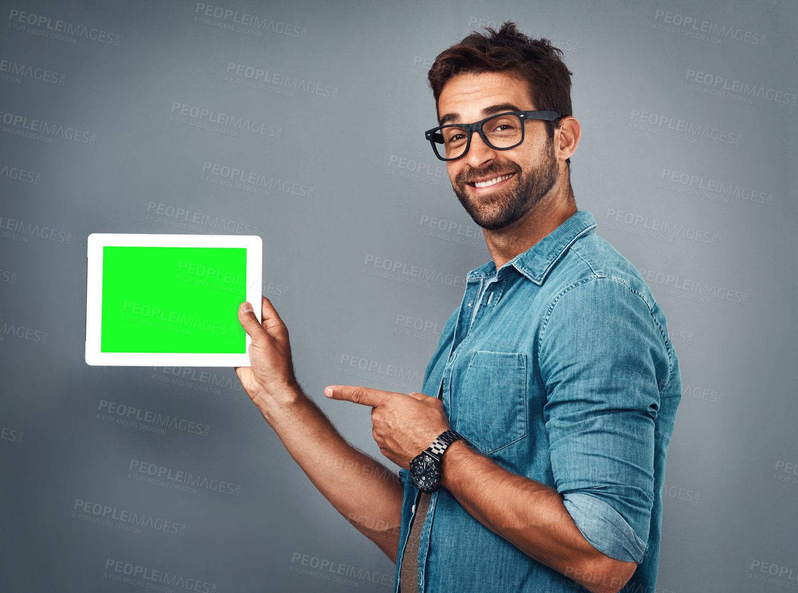 Buy stock photo Happy man, tablet and pointing to green screen for advertising against a grey studio background. Portrait of male person showing technology display, chromakey or mockup for copy space advertisement