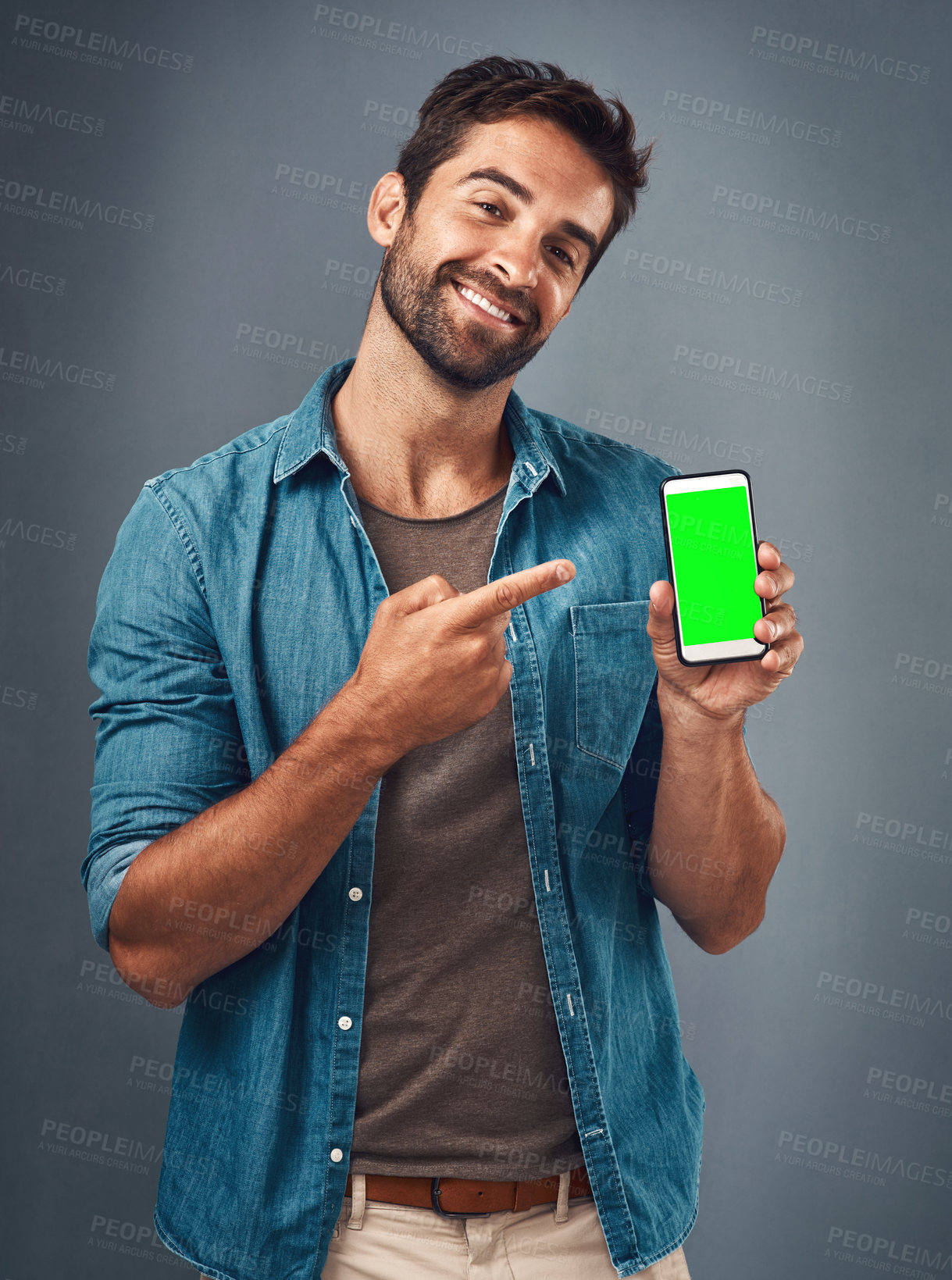 Buy stock photo Happy man, phone and pointing to mockup green screen for advertising against a grey studio background. Portrait of male person smiling and showing smartphone display or chromakey for advertisement