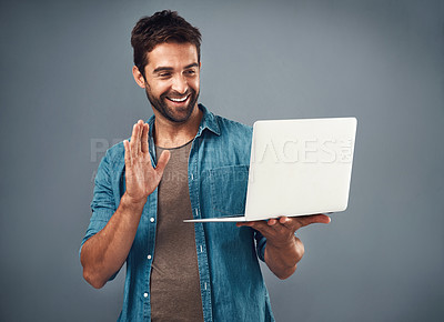 Buy stock photo Studio shot of a handsome young man using a laptop and waving against a grey background
