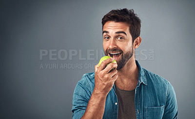 Buy stock photo Studio shot of a handsome young man eating an apple against a grey background