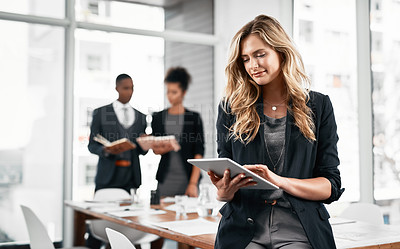 Buy stock photo Shot of a young businesswoman using a digital tablet in an office with her colleagues in the background