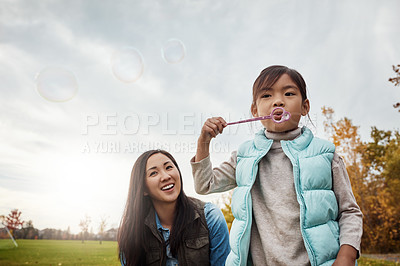 Buy stock photo Mom, daughter and blowing bubbles in park with smile for fun, playing and bonding with child development. Asian parent, woman and happy with kid in garden on break for care, support and trust