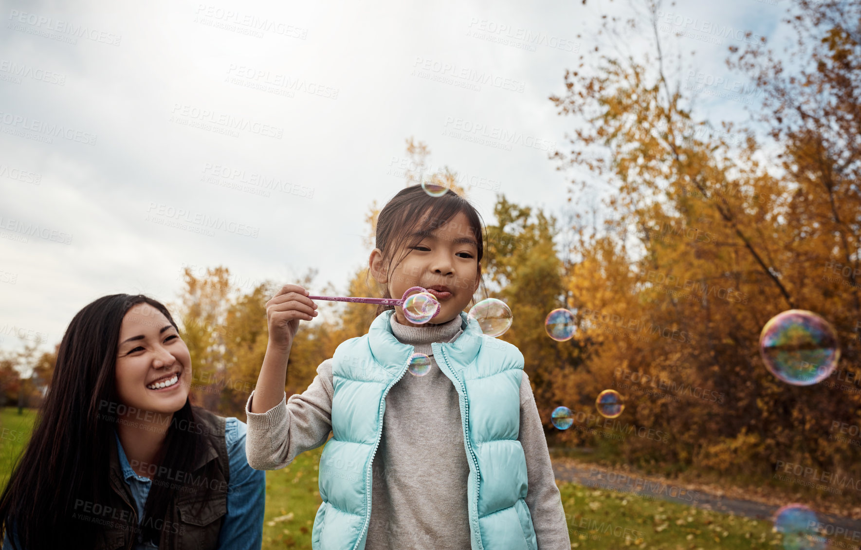 Buy stock photo Shot of a mother and her little daughter playing with bubbles outdoors