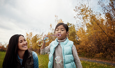 Buy stock photo Shot of a mother and her little daughter playing with bubbles outdoors